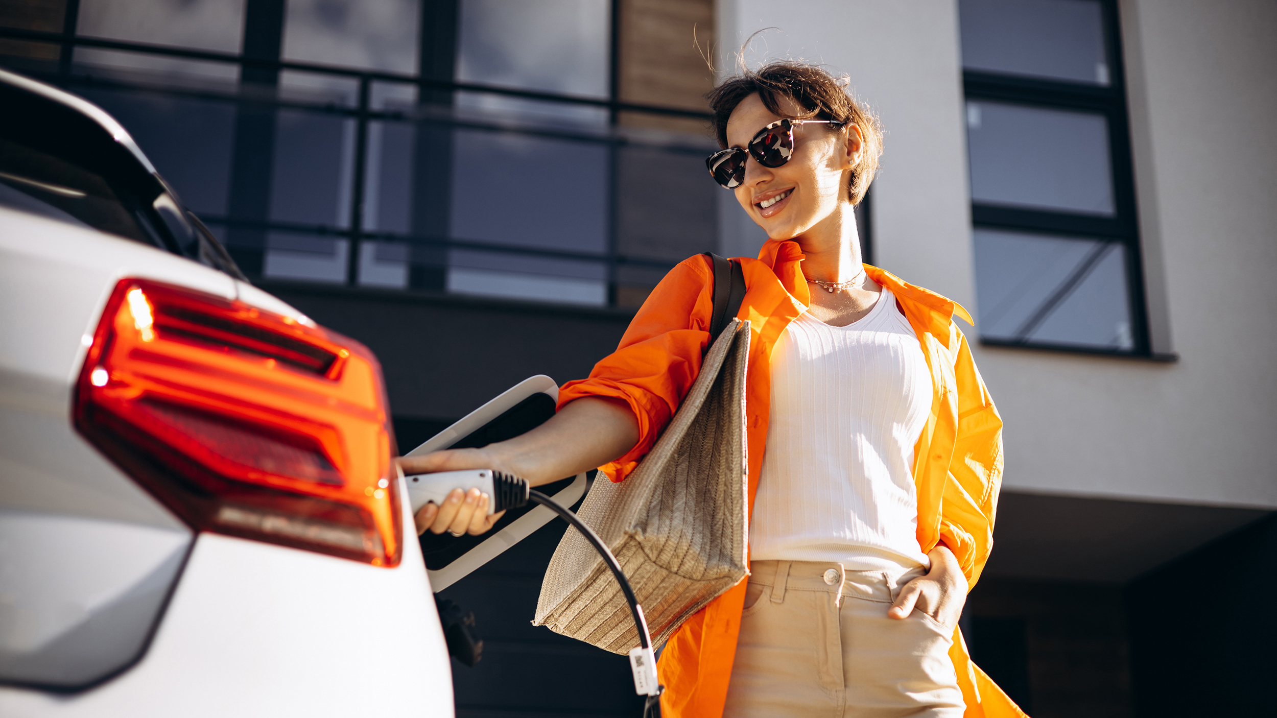 Eine Frau mit Sonnenbrille steckt ein weißes Elektroauto an.