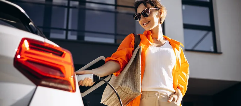 Eine Frau mit Sonnenbrille steckt ein weißes Elektroauto an.