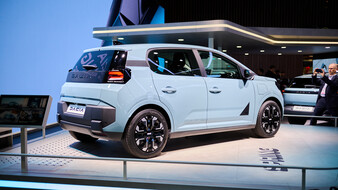 Hellblauer Dacia Spring schräg von hinten mit dunklem Band zwischen den Rückleuchten, grauen Stoßfängerelementen und schwarz-silbernen Rädern.