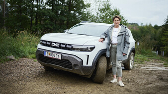 Dacia-CEO Katrin Adt steht neben einem weißen Auto, das im Schlamm steht.