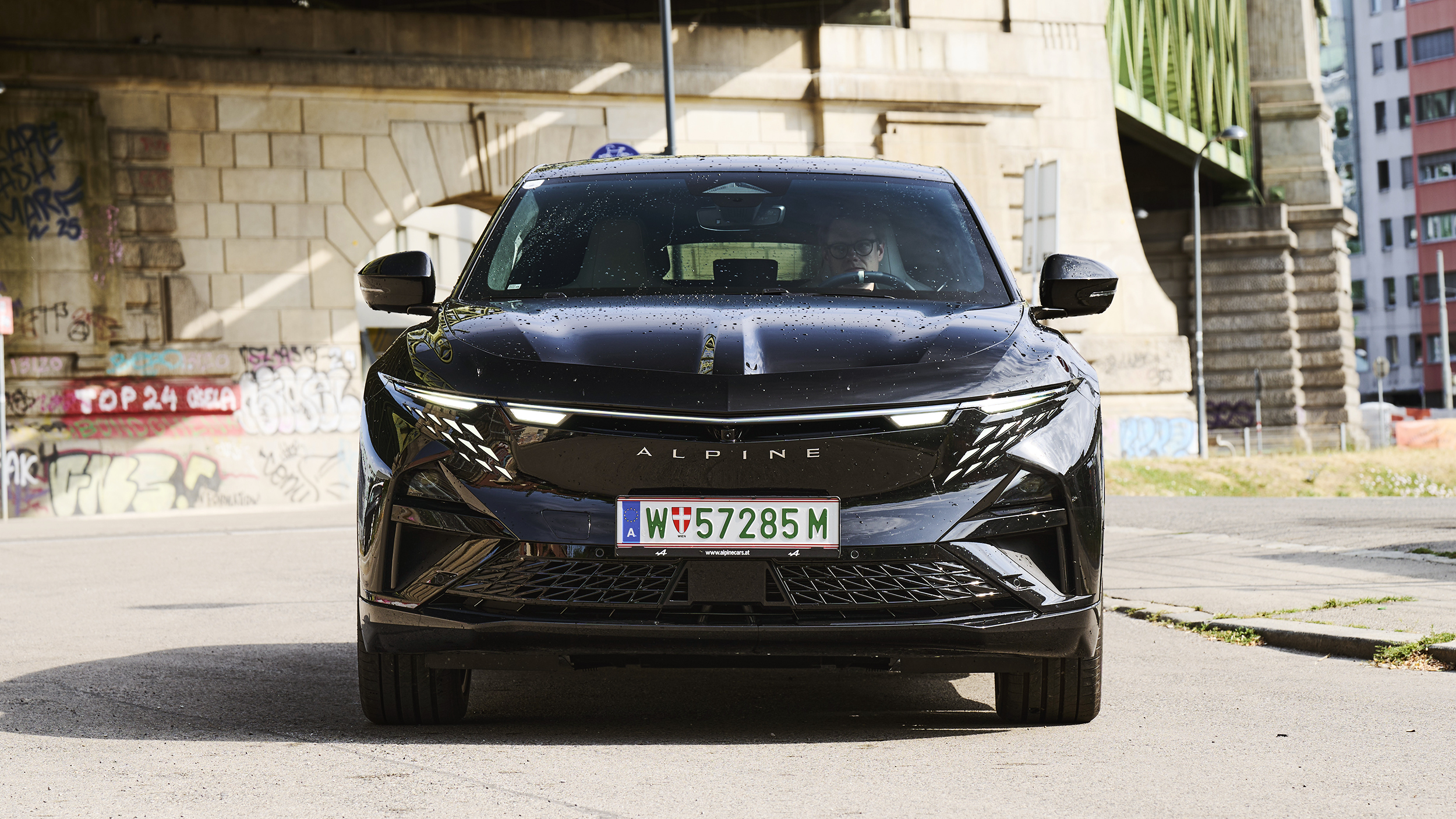 Front einer schwarzen Alpine A390 GT, die unter einer Brücke in der Stadt steht.