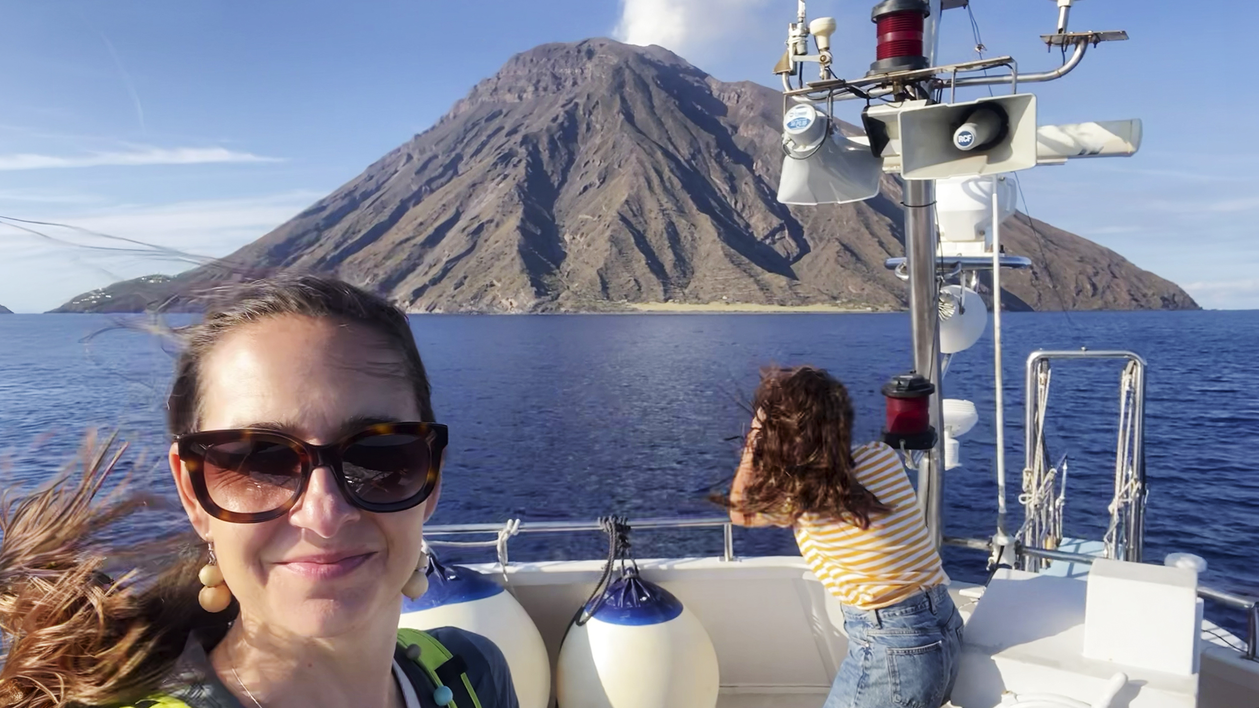 Frau fährt am Boot und hinter ihr liegt der Vulkan Stromboli.