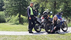 Auf dem Bild sieht man zwei Personen mit ihren Motorrädern. Ein Mann steht neben seinem Motorrad. Eine Frau kniet vor ihrem Bike.