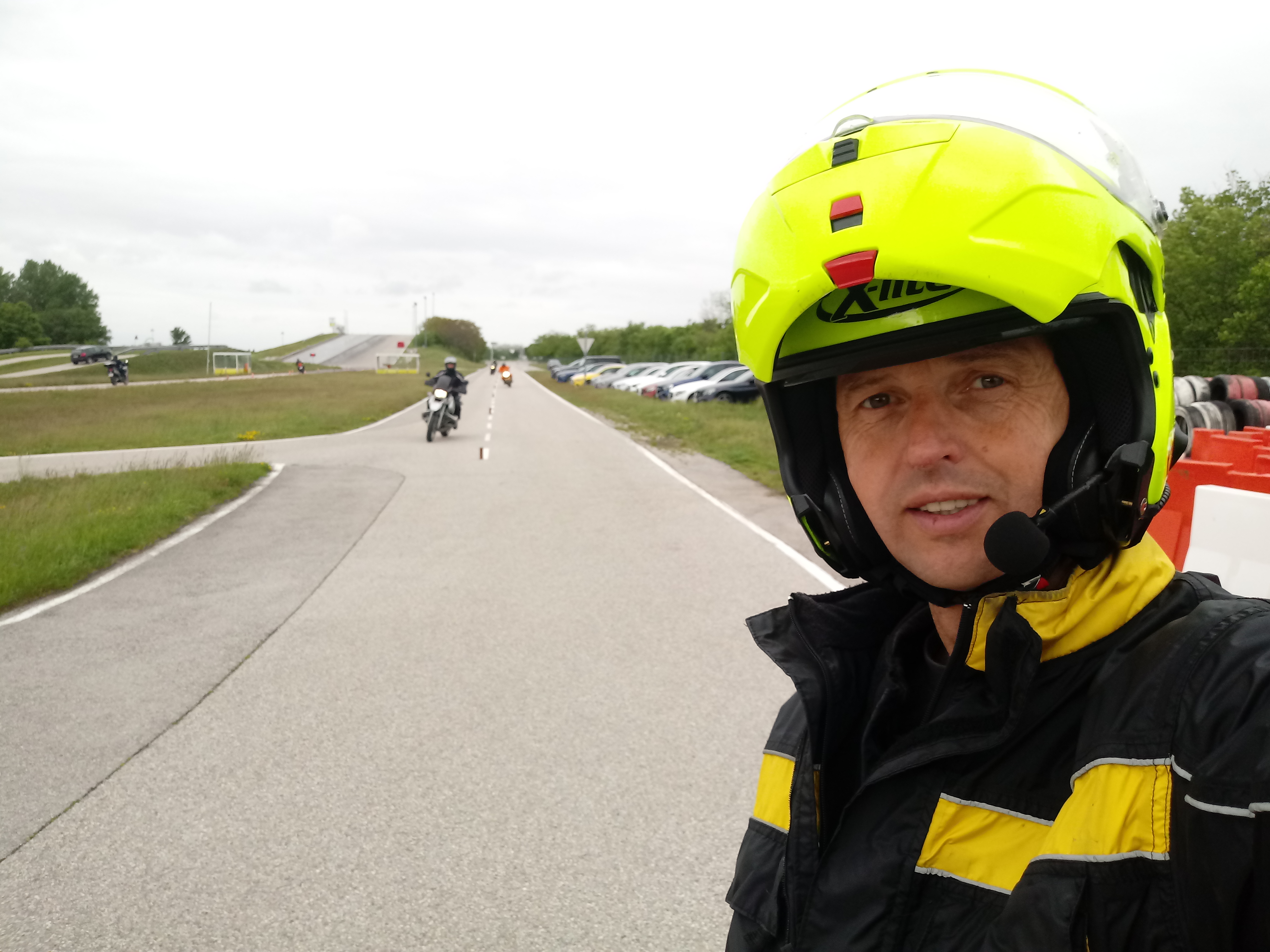 Das Foto zeigt einen Mann der auf einer Fahrstrecke steht mit einem gelben Helm und einem Headset. 