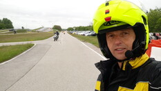 Das Foto zeigt einen Mann der auf einer Fahrstrecke steht mit einem gelben Helm und einem Headset.
