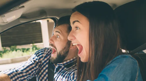 Es ist ein Mann und eine Frau zu sehen, die im Auto sitzen und erschrocken schauen.