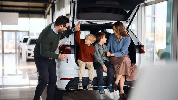 Eine fröhliche Familie mit zwei Söhnen sitzt im Kofferraum von einem weißen Neuwagen.