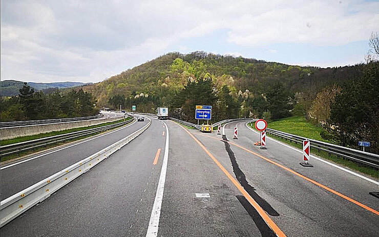Dreistreifige Autobahnbaustelle mit einer Betonleitwand und verengten Fahrstreifen.
