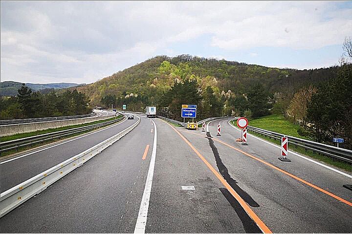 Dreistreifige Autobahnbaustelle mit einer Betonleitwand und verengten Fahrstreifen.