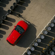 Ein Schmuckbild zum ÖAMTC-Sommerreifentest 2026: Eine Luftaufnahme, darauf mehrere Reihen übereinander gestapelter Autoreifen, dazwischen ein rotes Auto.