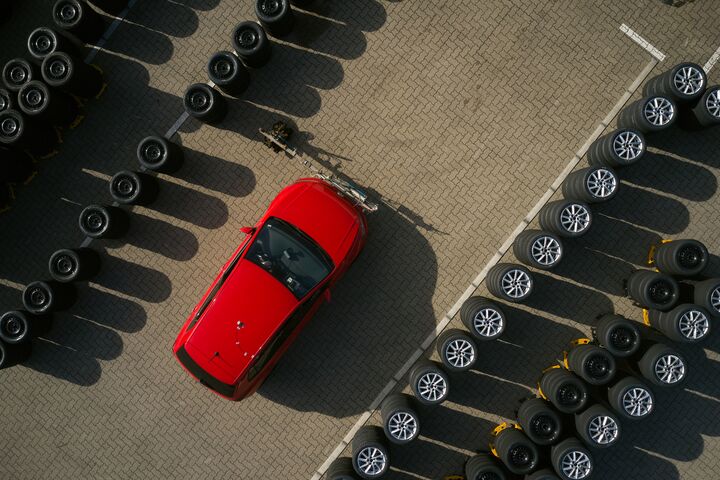 Ein Schmuckbild zum ÖAMTC-Sommerreifentest 2026: Eine Luftaufnahme, darauf mehrere Reihen übereinander gestapelter Autoreifen, dazwischen ein rotes Auto.