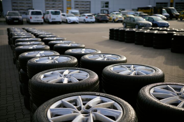 Ein Schmuckbild zum ÖAMTC-Sommerreifentest 2026: Zwei Reihen übereinander gestapelter Autoreifen vor einem Gebäude, vor dem Autos geparkt sind.