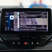 Auf dem Bild sieht man das Display in einem Auto. Auf dem Bildschirm ist die Planung einer Navigation zu sehen.