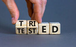 Symbol für bewährt und getestet. Geschäftsmann dreht Holzwürfel und ändert das Konzeptwort 'versucht' zu 'getestet' auf einem schönen grauen Hintergrund. Freier Platz für Text. Geschäfts- und bewährtes Konzept.