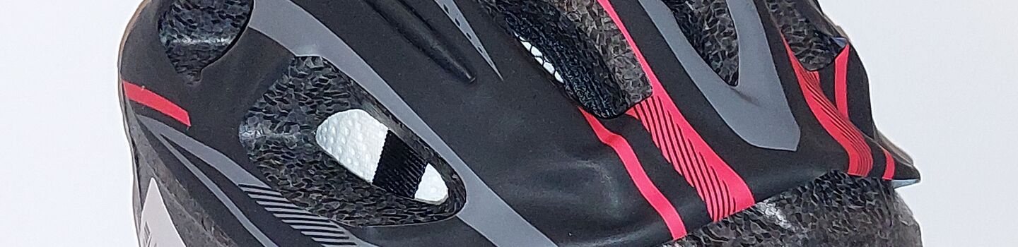 Kinderfahrradhelm in den Farben schwarz, grau, rot, isoliert vor grauem Hintergrund.