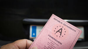 Ein alter rosa Papierführerschein aus Österreich, im Hintergrund ein Nummernschild