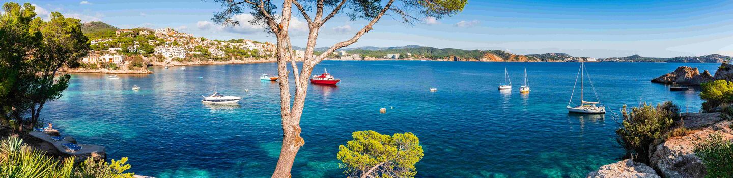 Auf dem Foto ist die Meeresbucht Cala Fornells auf Mallorca mit blauem Meer und einigen Segelschiffen und Motorbooten zu sehen.