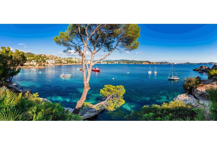 Auf dem Foto ist die Meeresbucht Cala Fornells auf Mallorca mit blauem Meer und einigen Segelschiffen und Motorbooten zu sehen.