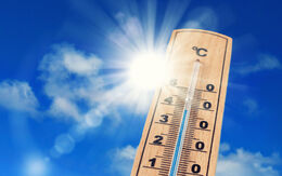 Ein altmodischer Thermometer vor blauem Himmel und strahlender Sonne.