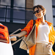 Eine Frau mit Sonnenbrille steckt ein weißes Elektroauto an.
