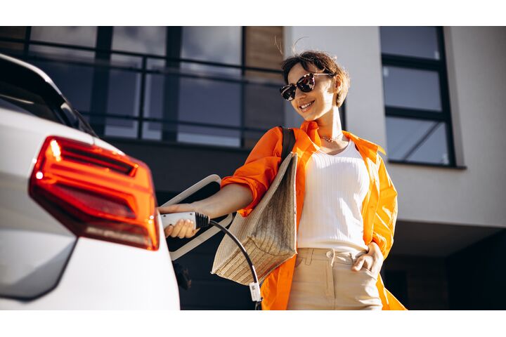 Eine Frau mit Sonnenbrille steckt ein weißes Elektroauto an.