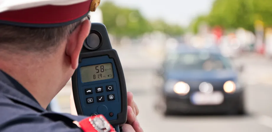 Ein Polizist misst mit einer Laserpistole die Geschwindigkeit eines schwarzen Autos.