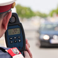Ein Polizist misst mit einer Laserpistole die Geschwindigkeit eines schwarzen Autos.
