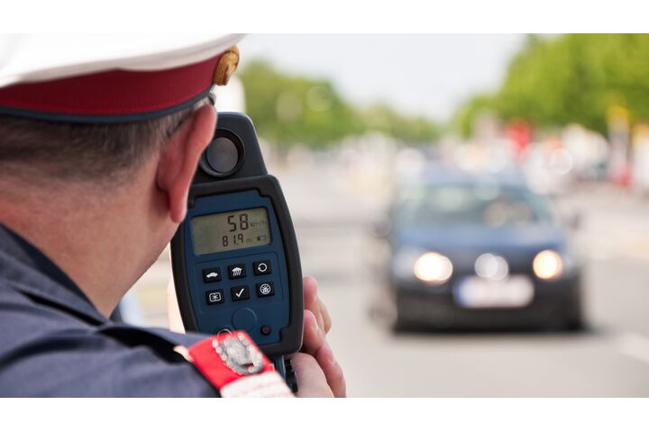 Ein Polizist misst mit einer Laserpistole die Geschwindigkeit eines schwarzen Autos.