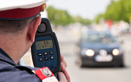Ein Polizist misst mit einer Laserpistole die Geschwindigkeit eines schwarzen Autos.