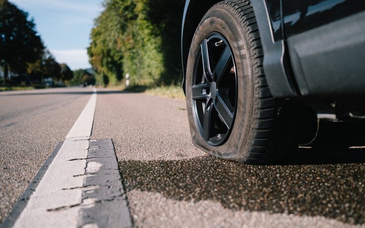 Betrug im Ausland – Vorsicht vor Trickbetrüger:innen Ein kaputter Vorderreifen am Auto, das Fahrzeug steht am Straßenrand.