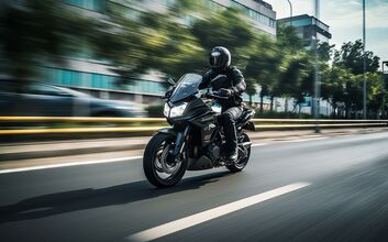 Ein Motorradfahrer in der Stadt, mit Helm und vollständiger Ausrüstung, fährt auf einer Straße. Im Hintergrund ein großes Bürogebäude und Bäume.