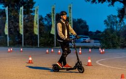 Ein junger Mann fährt auf einem E-Tretroller, auch E-Scooter genannt, zwischen Leitkegeln bzw. Pylonen auf dem Testgelände in einem ÖAMTC Fahrtechnik Zentrum.