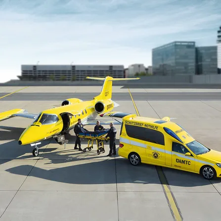ÖAMTC Ambulanzjet und ÖAMTC Rettungsfahrzeug stehen am Flugfeld. Drei Personen in der Mitte.
