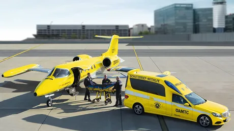ÖAMTC Ambulanzjet und ÖAMTC Rettungsfahrzeug stehen am Flugfeld. Drei Personen in der Mitte.
