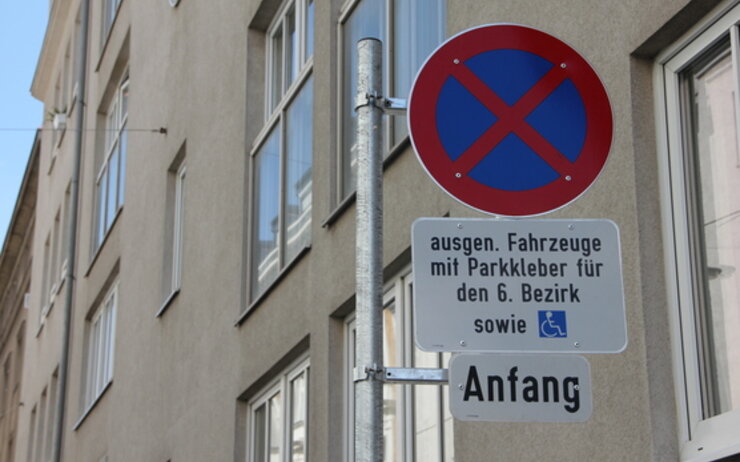 Das Bild zeigt ein Parkverbotsschild mit zwei Zusatztafeln in Wien. Auf dem oberen Zusatzschild steht: "ausgen. Fahrzeuge mit Parkkleber für den 6. Bezirk sowie" und zeigt ein Symbol für einen Behindertenparkplatz. Das untere Zusatzschild zeigt das Wort "Anfang“.