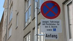 Das Bild zeigt ein Parkverbotsschild mit zwei Zusatztafeln in Wien. Auf dem oberen Zusatzschild steht: "ausgen. Fahrzeuge mit Parkkleber für den 6. Bezirk sowie" und zeigt ein Symbol für einen Behindertenparkplatz. Das untere Zusatzschild zeigt das Wort "Anfang“.