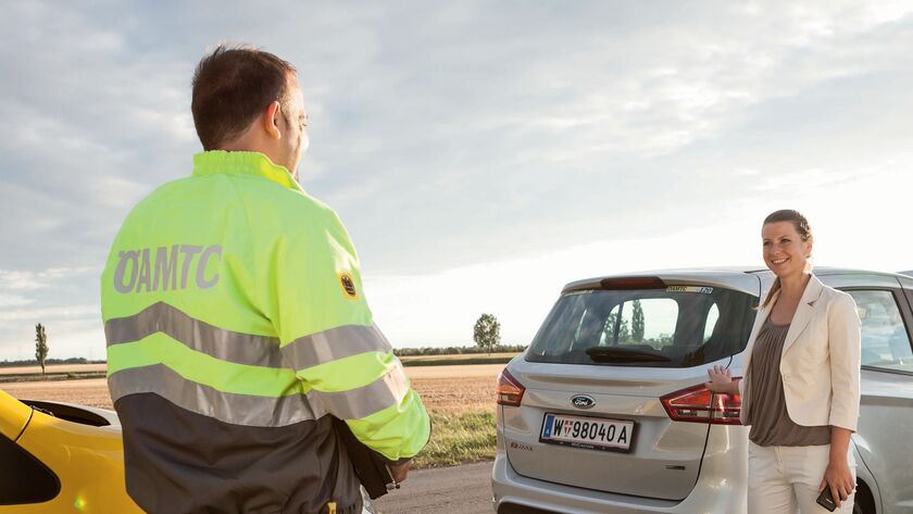 Ein ÖAMTC-Pannenhelfer, der einer Autofahrerin bei einer Panne hilft, mit einem Fahrzeug im Hintergrund.