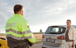 Ein ÖAMTC-Pannenhelfer, der einer Autofahrerin bei einer Panne hilft, mit einem Fahrzeug im Hintergrund.