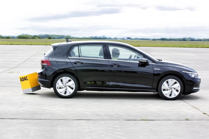 Ein schwarzes Auto am Testgelände übersieht einen gelben Kartonwürfel und berührt ihn hinten mit der Stoßstange. Der Hintergrund des Bildes zeigt eine weite, leere Landschaft mit einem bewölkten Himmel.
