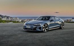 Audi e-Tron Sportwagen in blaugrau steht auf einer Straße. Im Hintergrund eine Stadt am Meer und Küste sichtbar.