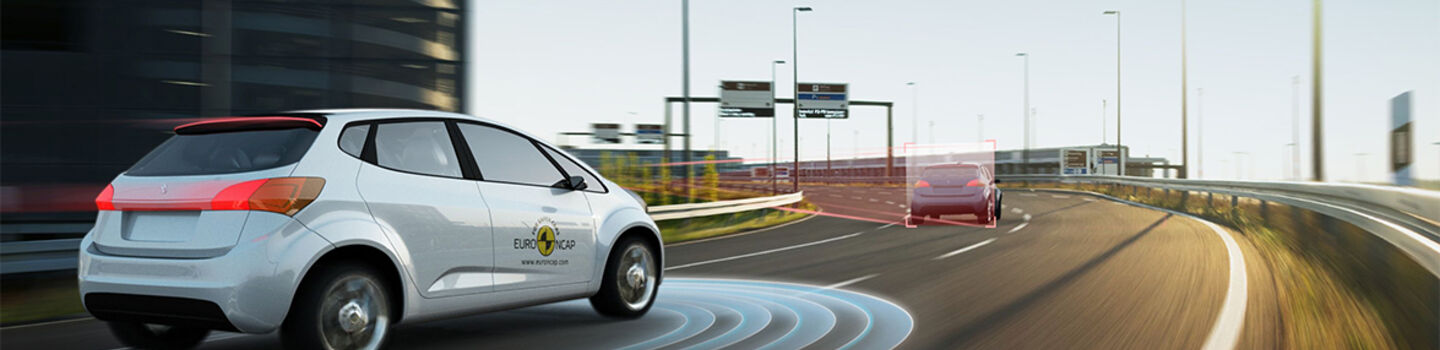 Ein EURO NCAP-Testauto fährt auf der Autobahn vor einer Linkskurve hinter einem Auto her. Der Kurvenradius wird im Bild grafisch angezeigt.