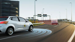 Ein EURO NCAP-Testauto fährt auf der Autobahn vor einer Linkskurve hinter einem Auto her. Der Kurvenradius wird im Bild grafisch angezeigt.