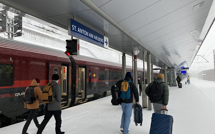 Menschen am Bahnsteig von Sankt Anton am Arlberg. Im Hintergrund ein Railjet