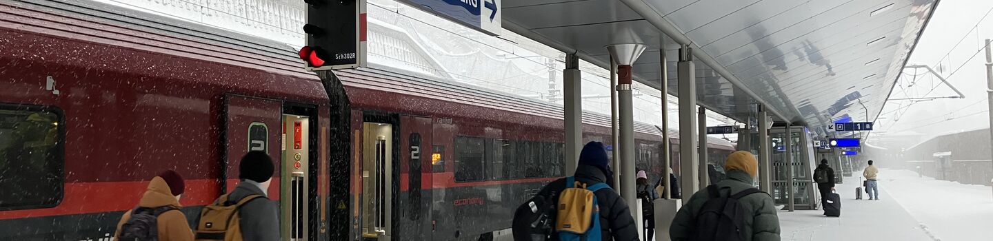 Menschen am Bahnsteig von Sankt Anton am Arlberg. Im Hintergrund ein Railjet