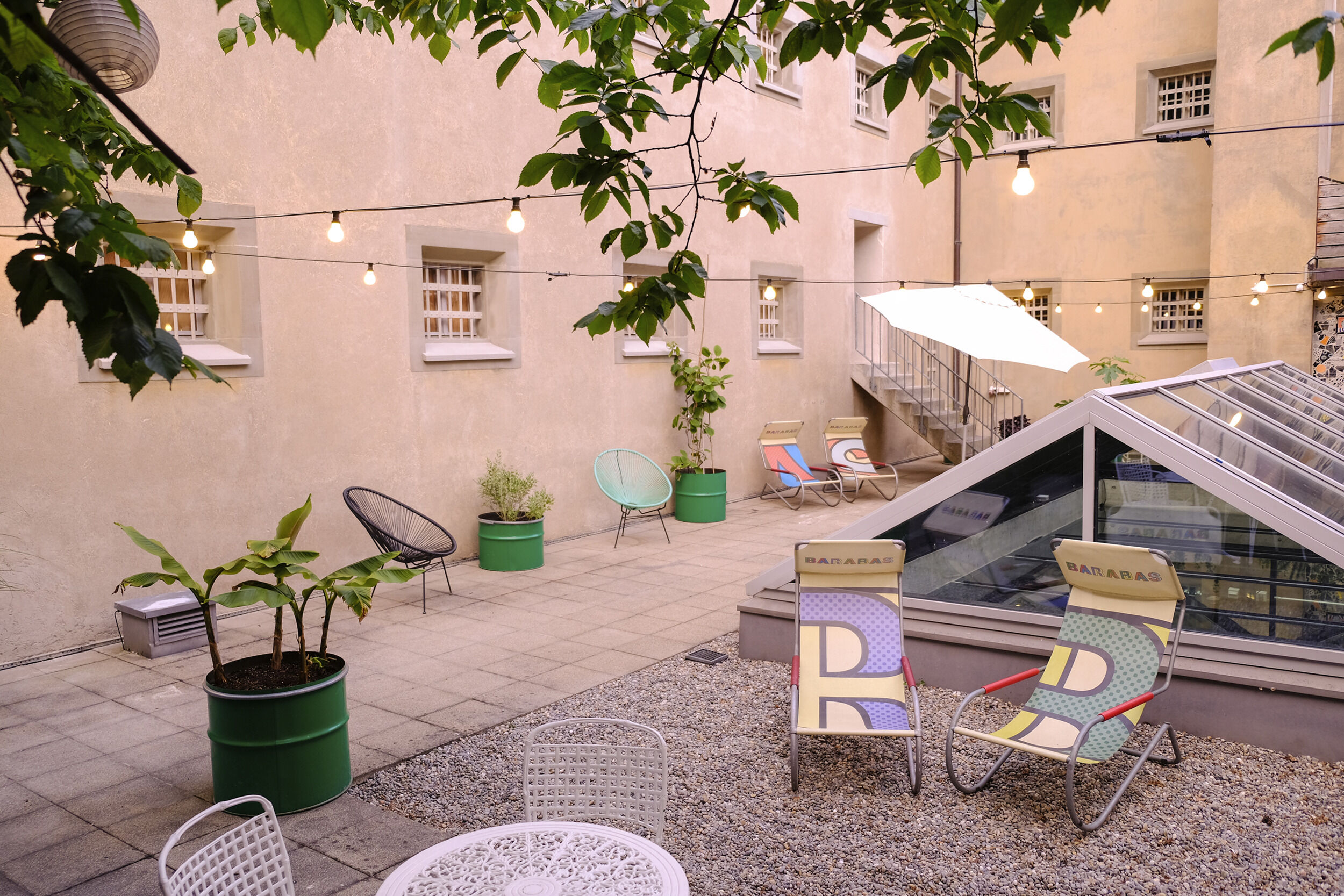 Ein Innenhof mit verschiedenen Stühlen, Pflanzen in grünen Töpfen und Lichterketten.