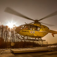 Christophorus-Notarzthubschrauber, der gerade abhebt oder landet. Die Sonne steht tief am Himmel und erzeugt eine warm-goldene Beleuchtung, während die Rotorblätter des Hubschraubers sich drehen.