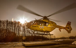 Christophorus-Notarzthubschrauber, der gerade abhebt oder landet. Die Sonne steht tief am Himmel und erzeugt eine warm-goldene Beleuchtung, während die Rotorblätter des Hubschraubers sich drehen.