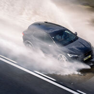 Ein Cupra der ÖAMTC Fahrtechnik fährt mit hoher Geschwindigkeit über eine nasse Fahrbahn