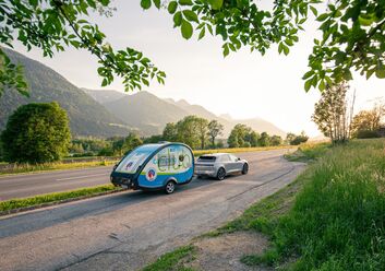 Es ist ein Straße bei Sonnenuntergang zu sehen. Es fährt ein Auto mit dem ÖCC-Campinganhänger.