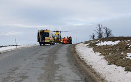 Der Christophorus 2-Hubschrauber, ein gelber Krankenwagen und Einsatzkräfte auf einer Landstraße bei einem Unfall. Am Straßenrand sieht man noch Schneereste.